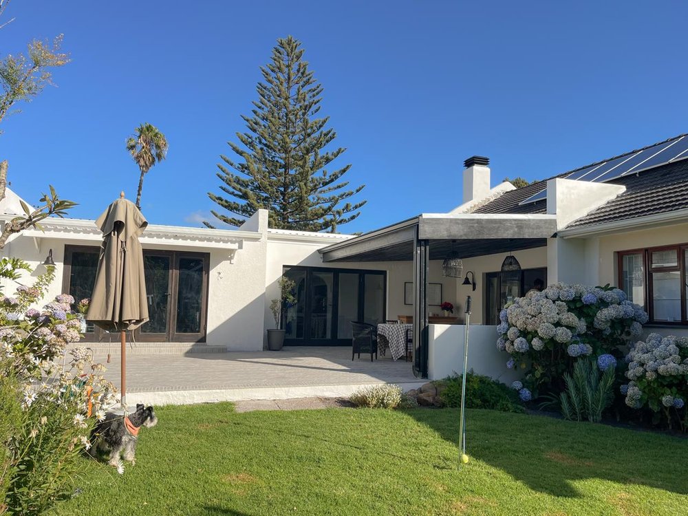 Wide exterior view of the back garden and covered patio, with a dog on the lawn