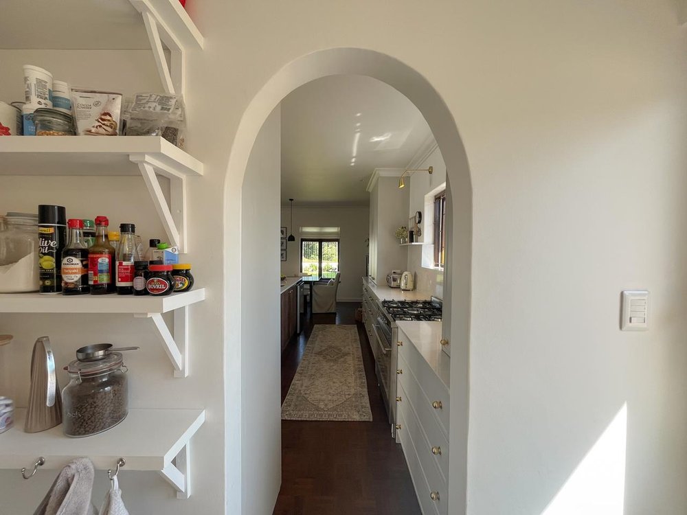 Pantry with open shelving, seen through an arched doorway
