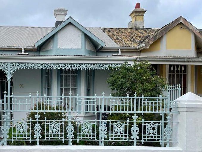 The front of a Victorian terrace house with an ornate pale green cast-iron fence and lace verandah trim