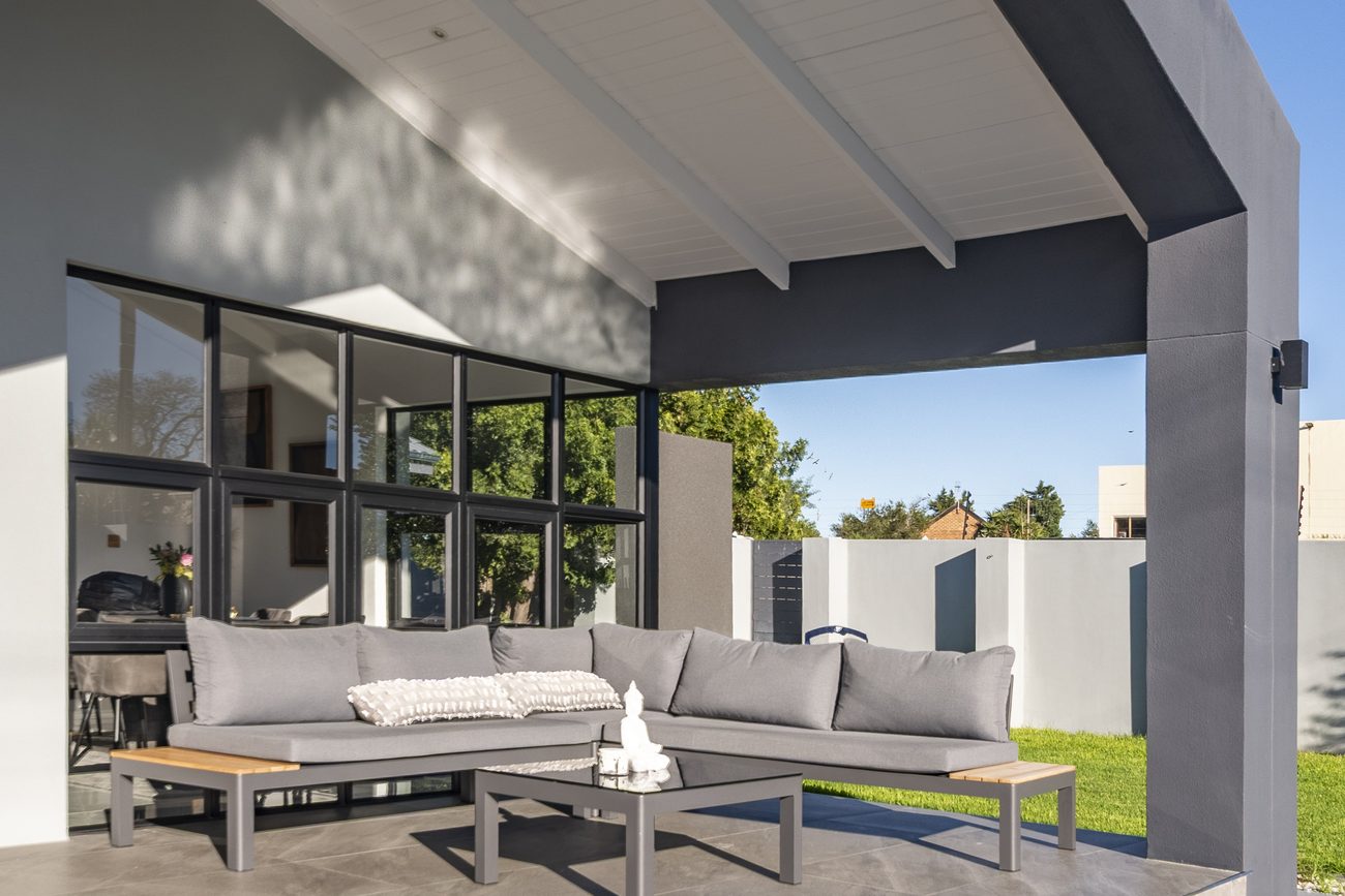 A covered patio with a lounge suite, black steel windows and wide steps down to the lawn