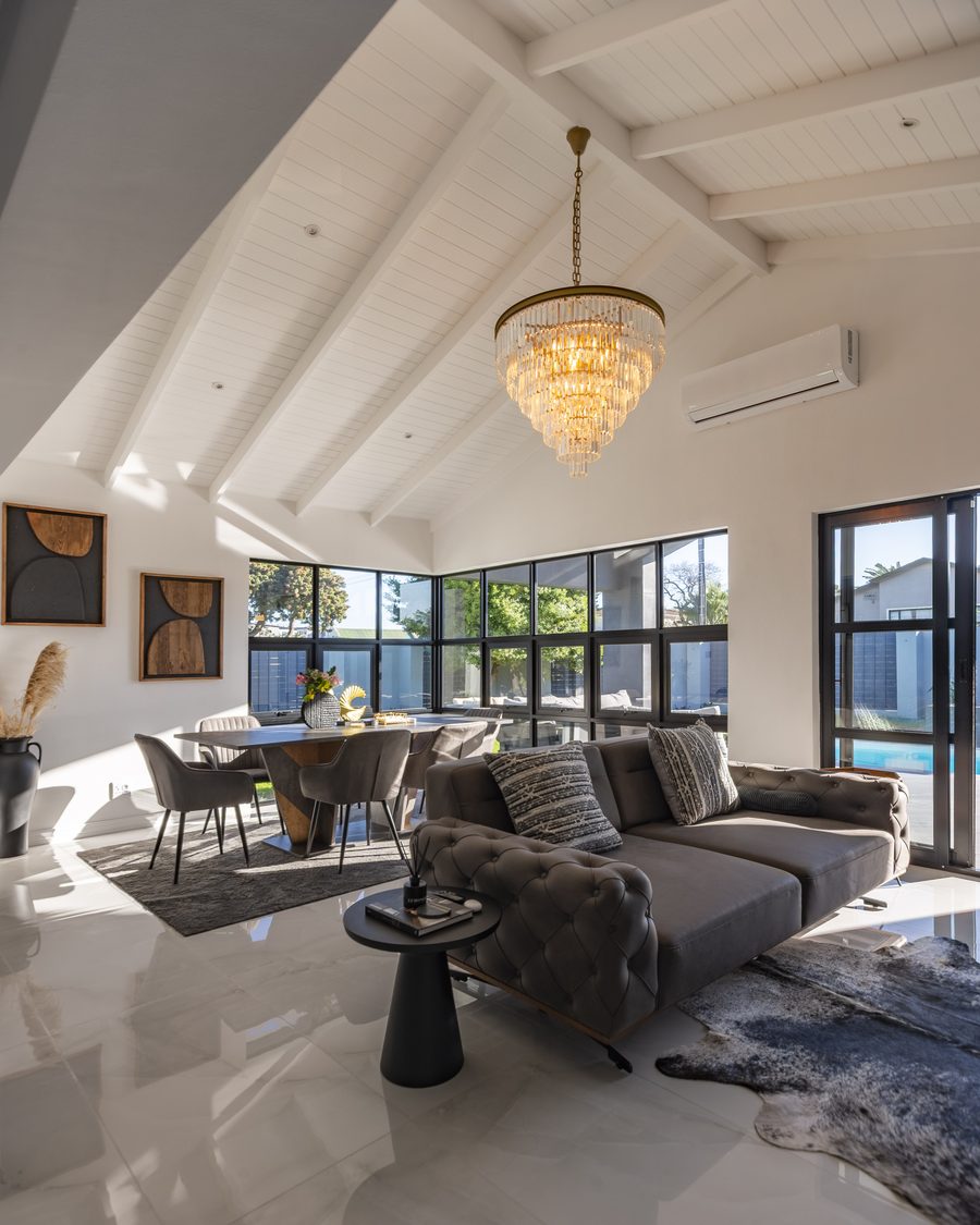 An open-plan living space with a white timber-lined vaulted ceiling, a crystal chandelier, black-framed glazing and polished floors